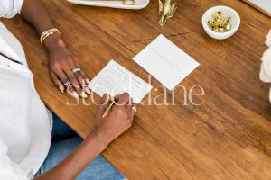 Horizontal stock photo of a woman sitting at her desk writing a note.