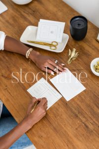 Vertical stock photo of a woman sitting at her desk writing a note.