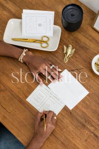 Vertical stock photo of a woman sitting at her desk writing a note.