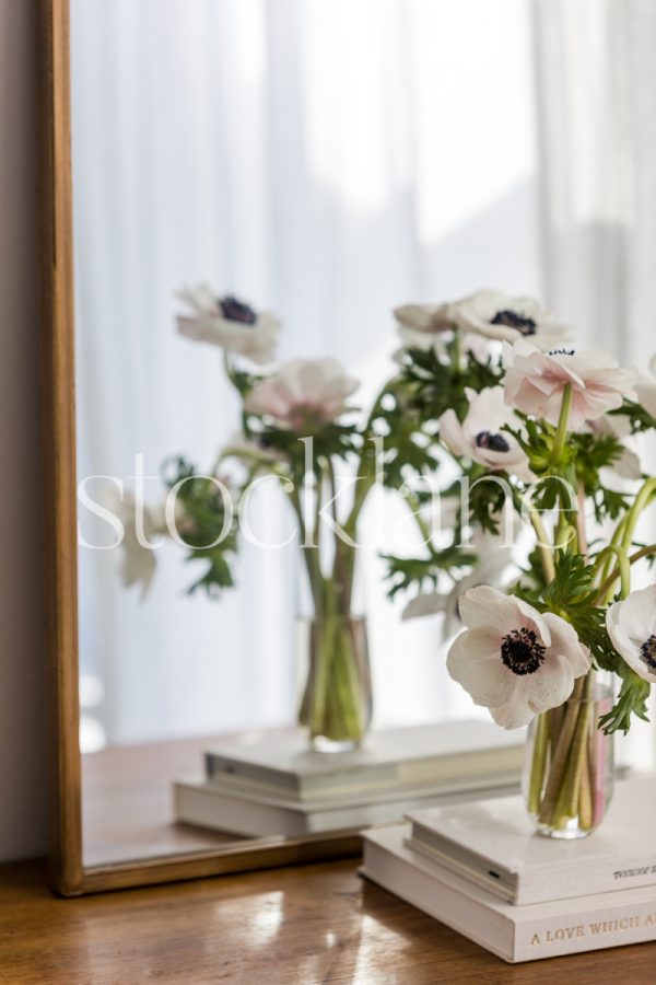 Vertical stock photo of a vase with flowers on top of neutral colored books.