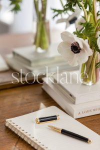 Vertical stock photo of a vase with flowers on top of neutral colored books.