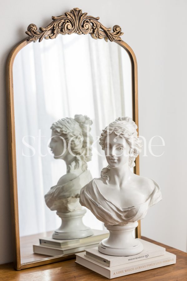 Vertical stock photo of a table and a sculpture of a woman on top of books.