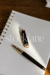 Vertical stock photo of a notebook and a pen on a wood desk.